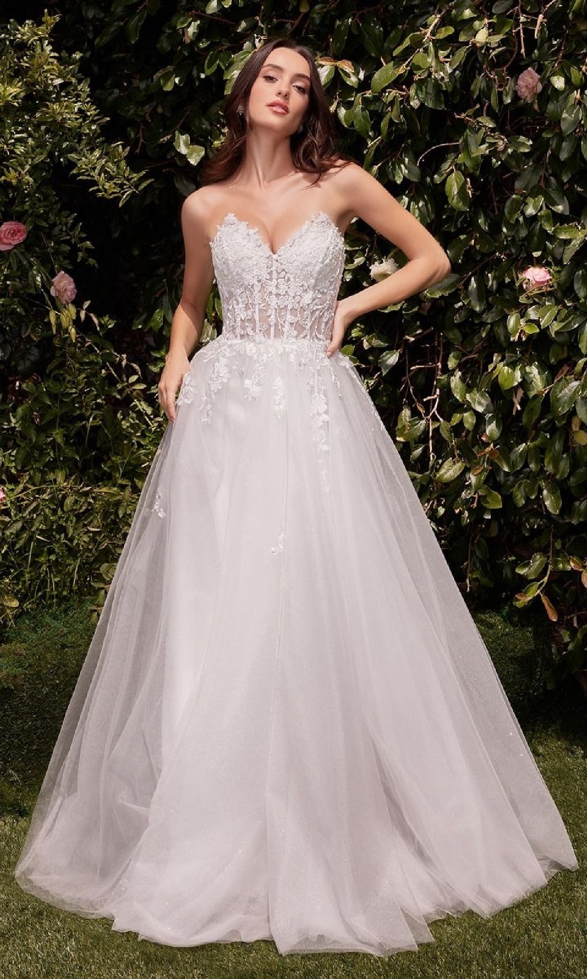 A woman stands outdoors before greenery, wearing the Ladivine C148W—an elegant strapless long white wedding gown featuring a fitted lace bodice and a flowing tulle skirt.